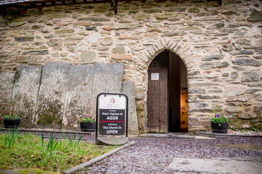 A bilingual sign welcomes people into an old stone church