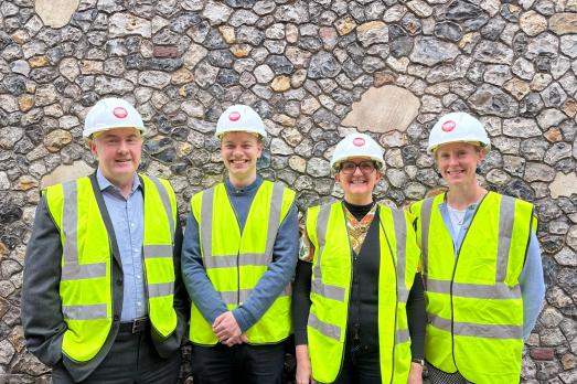 Four smiling people in yellow high vis jackets and white hard hats