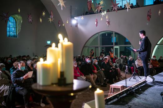 Candles at the forefront with a man preaching to congregation