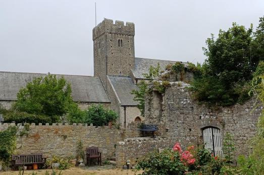A large grey stone church with a tower in the middle. Some of the garden and flowers are visible.