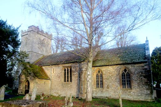 A warm stoned church with a tower on the left hand side of the image. A free is visible in the foreground.