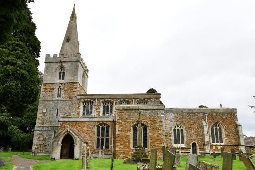A yellow stone historic church in Leicestershire. A tower and pointed spire is on the left hand side of the image.