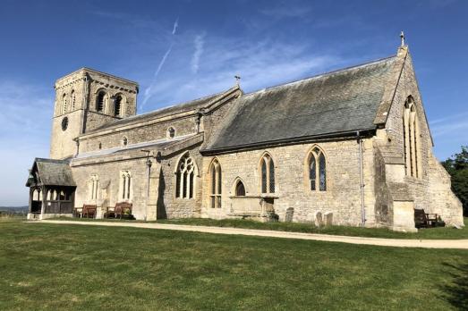 A landscape photograph of St Mary, a warm stone coloured building with the tower on the far left-hand-side 