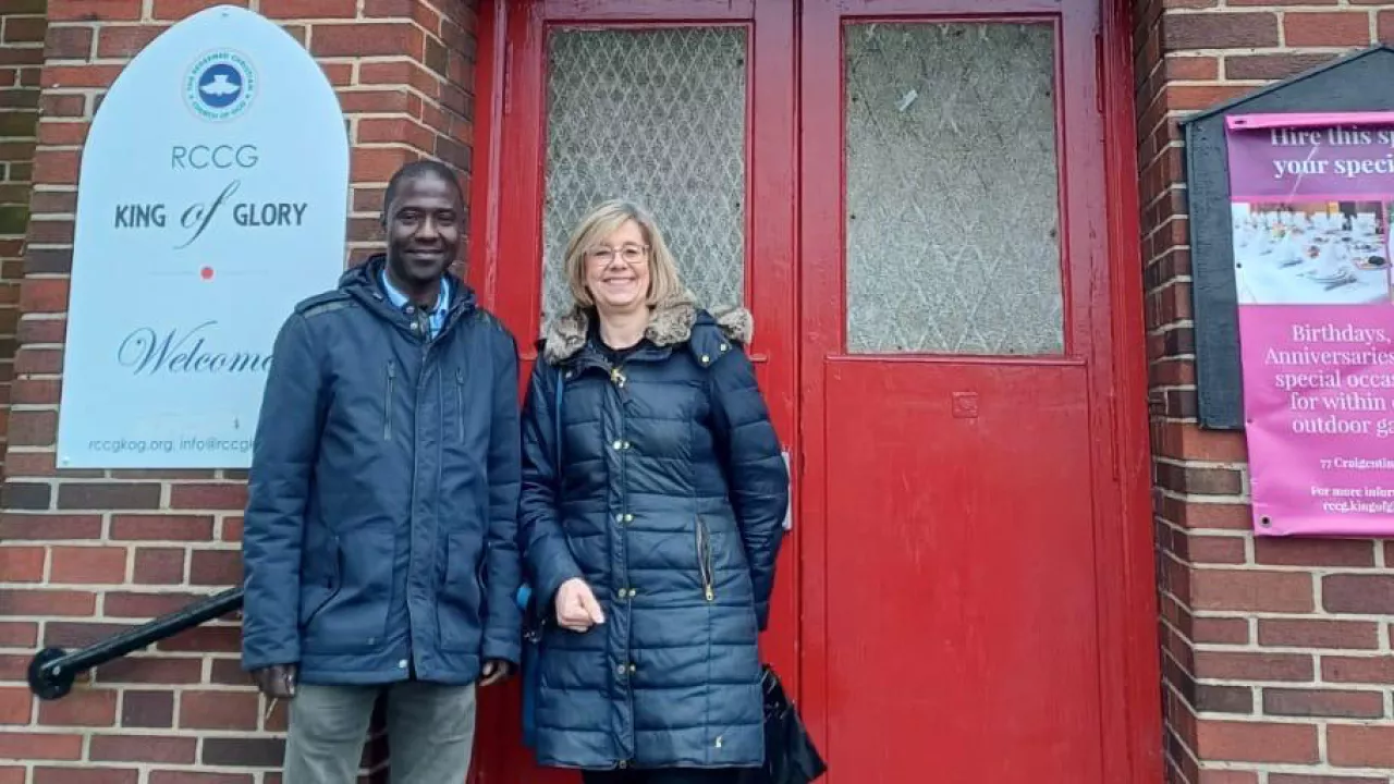 A photograph of two people standing outside the front door of a church