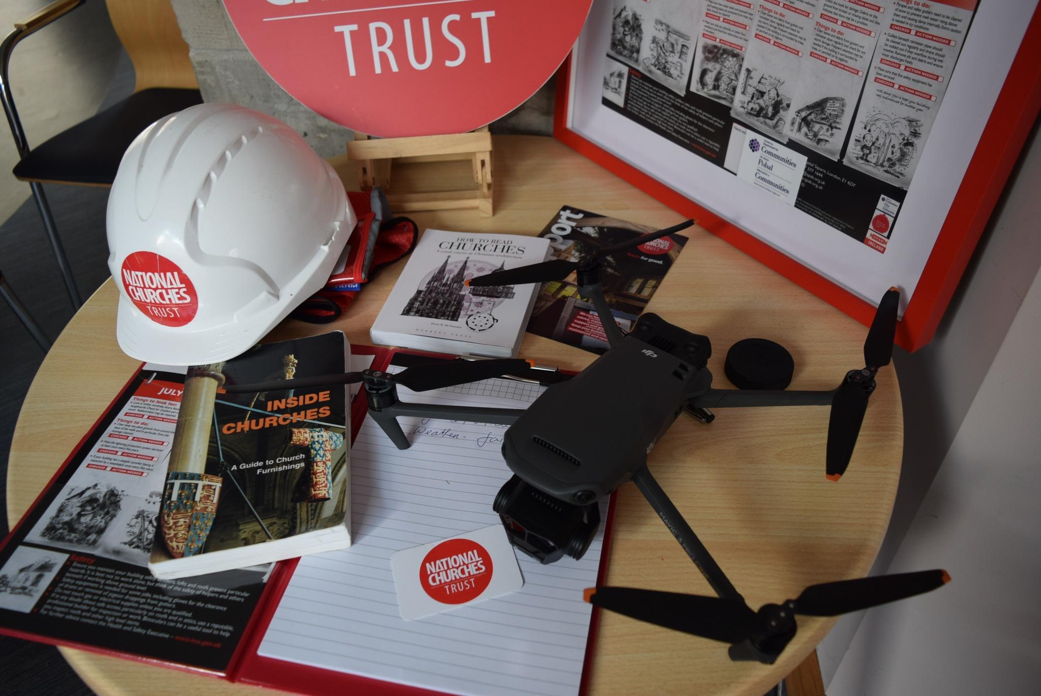 A table feature literature that helps to keep historic churches open. There is also a hard hat with the National Churches Trust logo and a drone.