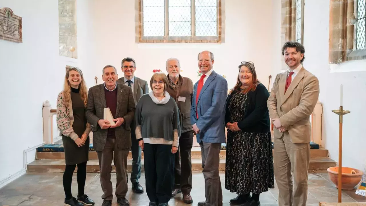 eight people stand together. National Churches staff and Chair with the team at St James the Great who are holding their 'Church of the Year' trophy. Everyone is smiling.