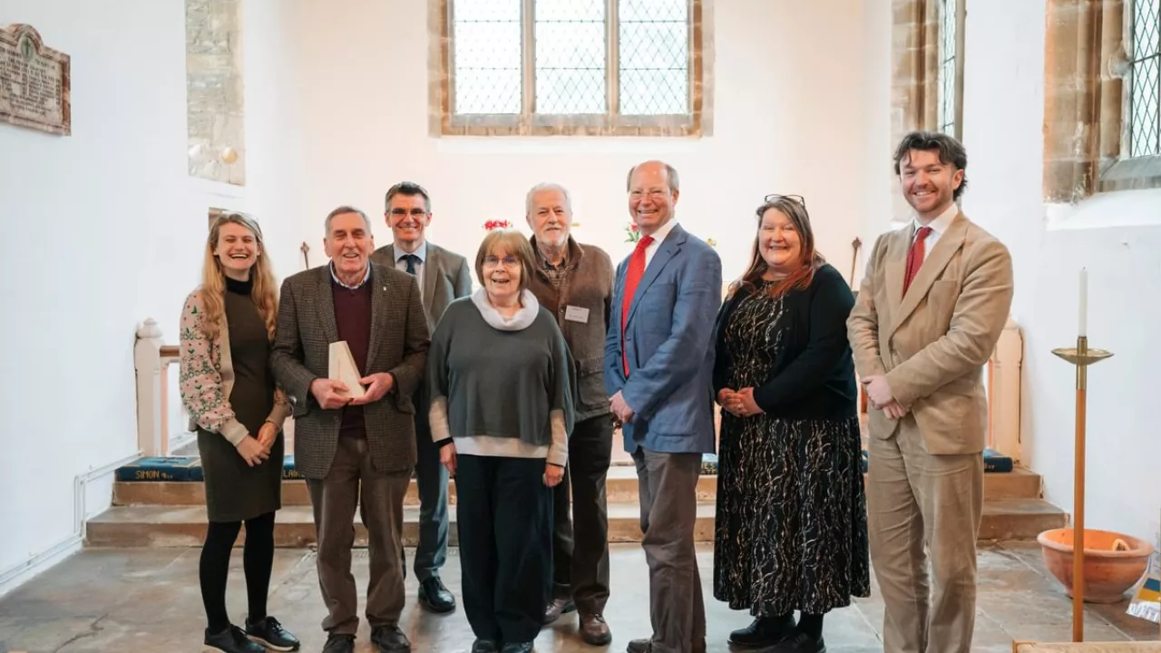 eight people stand together. National Churches staff and Chair with the team at St James the Great who are holding their 'Church of the Year' trophy. Everyone is smiling.