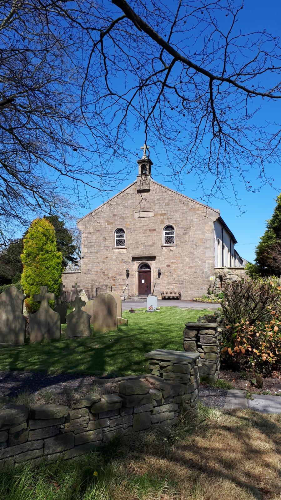The exterior of St Francis Hill Chapel, shown from a distance with greenery and trees in the foreground.