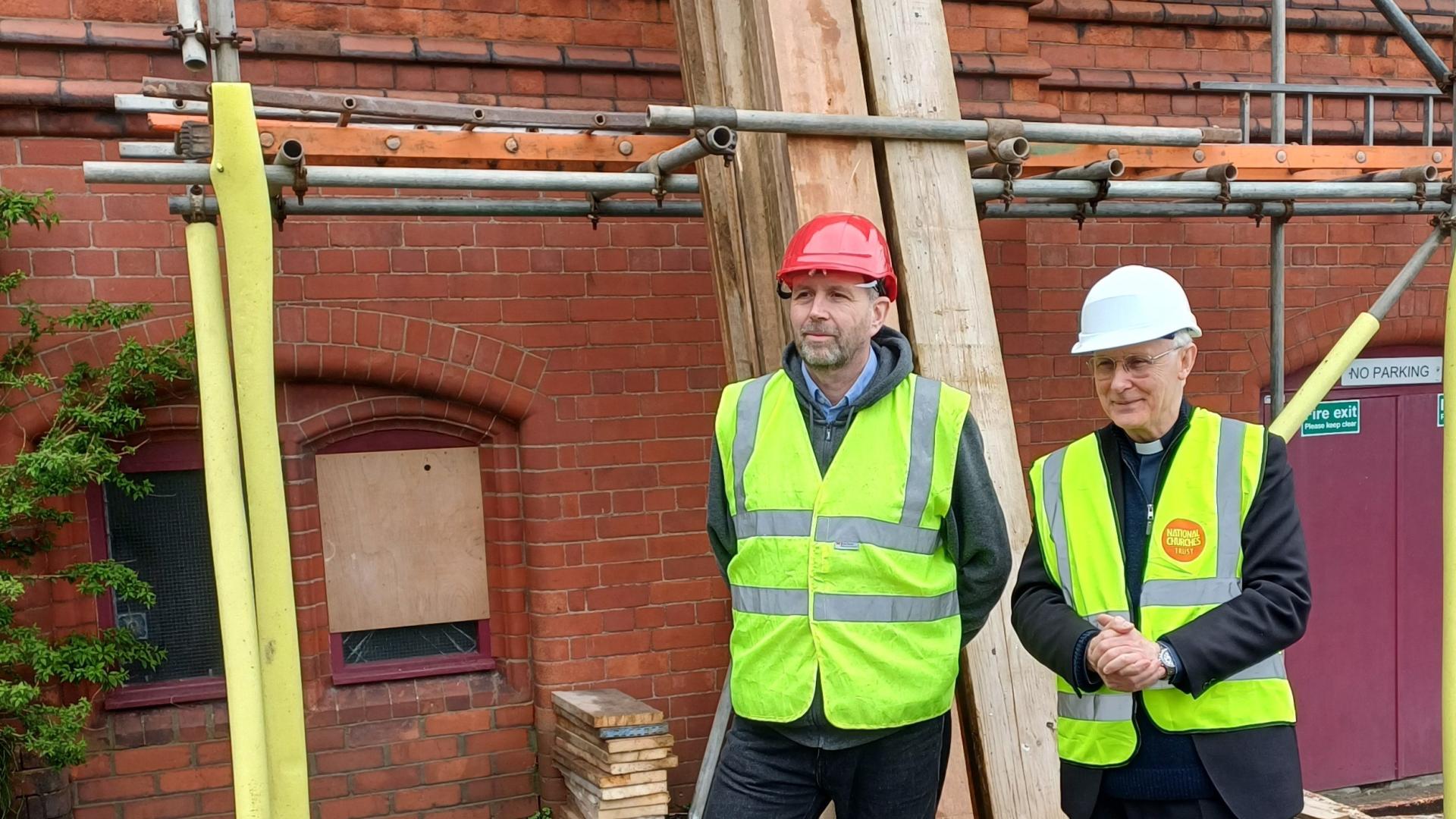 Two workers stood next scaffolding outside a red brick church