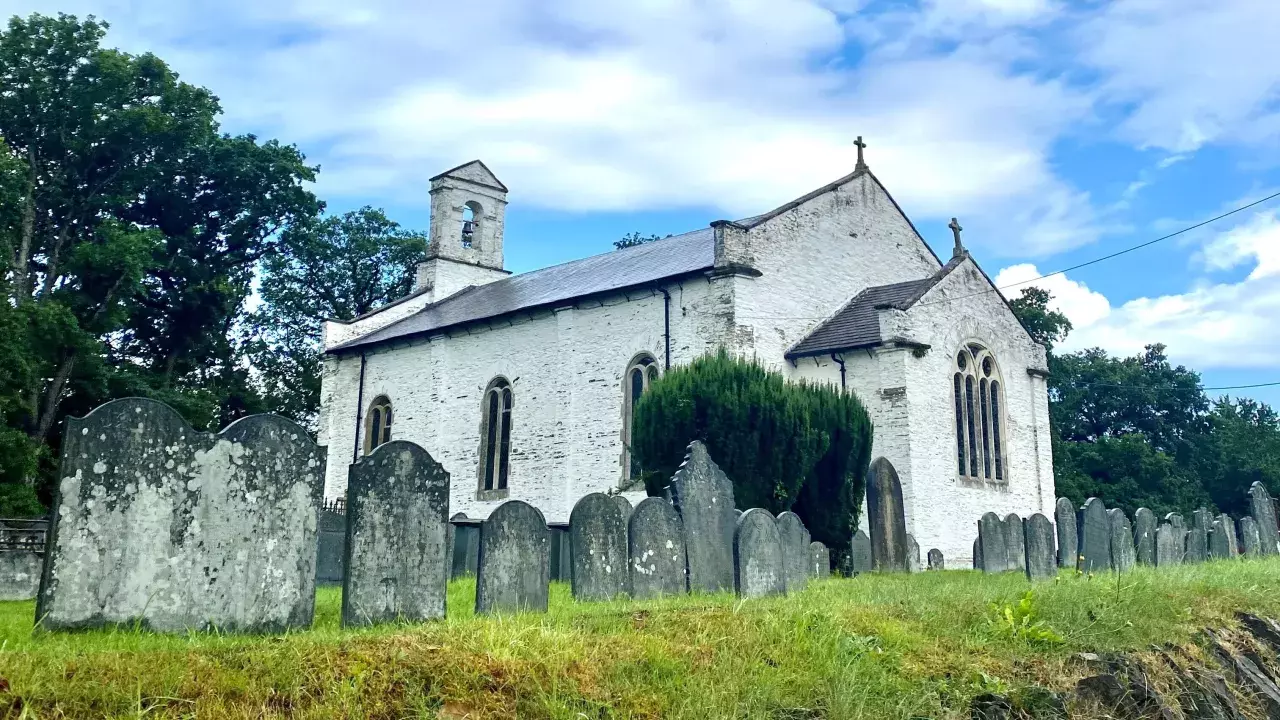 A white Welsh church with gravestones surrounding it
