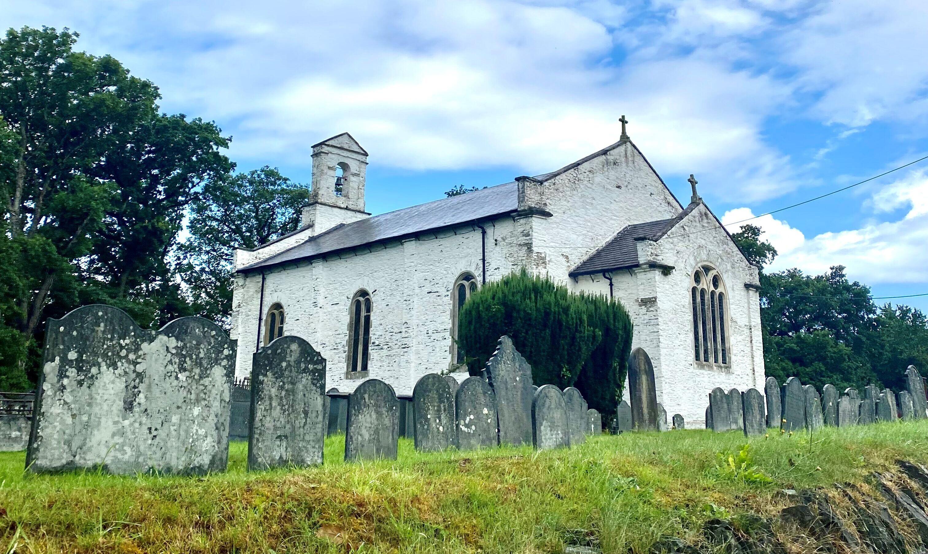 A white Welsh church with gravestones surrounding it