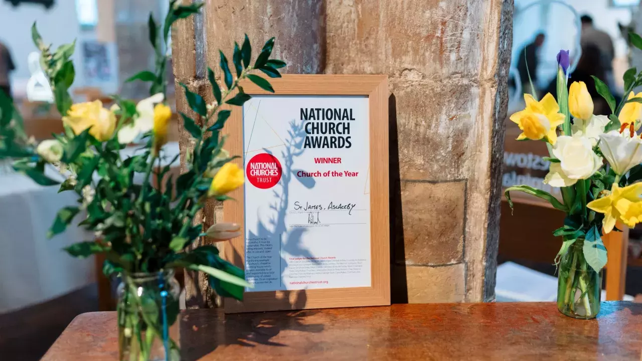 A wooden table with a certificate displayed, which congratulates St James the Great as the Church of the Year 2024