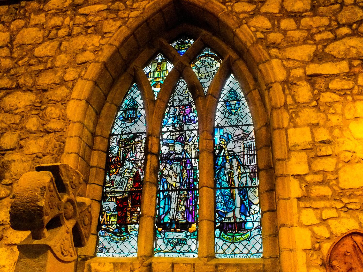 A colourful arched stained glass window surrounded by stone