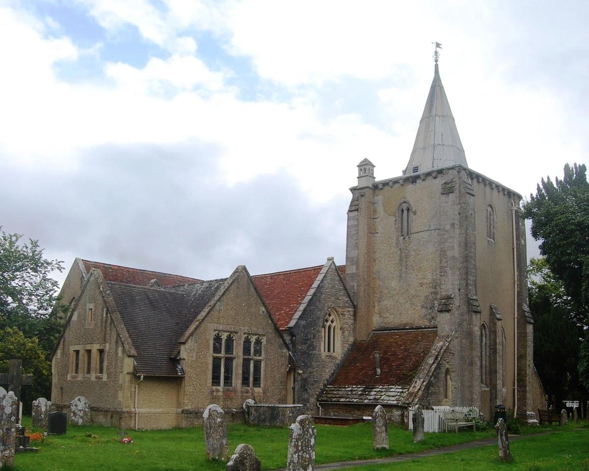 A large stone church with a red roof and prominent square tower on the left-hand side of the image. Photographed on a cloudy yet sunny day. 