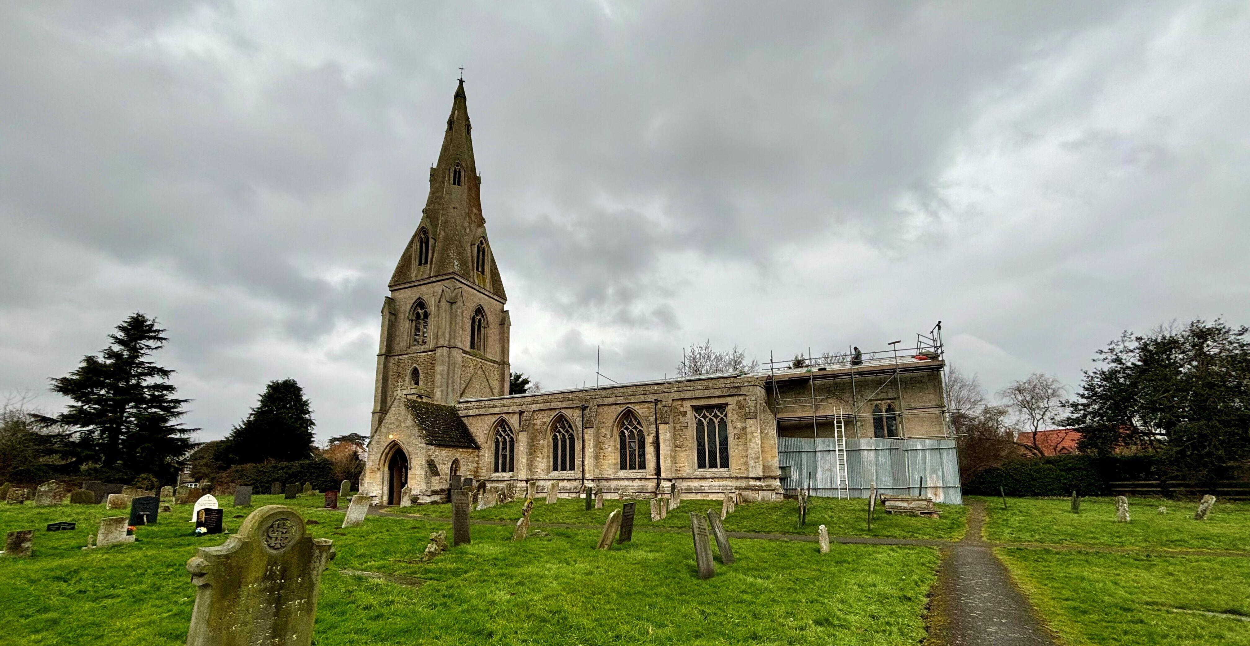 A beautiful stone church, St Peter Ad Vincula, photographed on a rainy day with men working on replacing the roof.