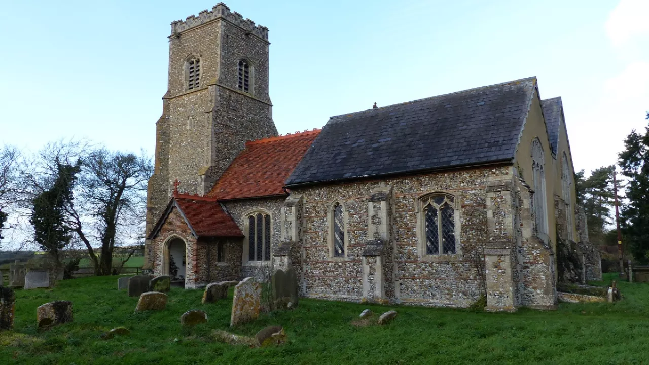 Exterior of St Margaret; a beautiful stone church with a tower on the left and a red roof.