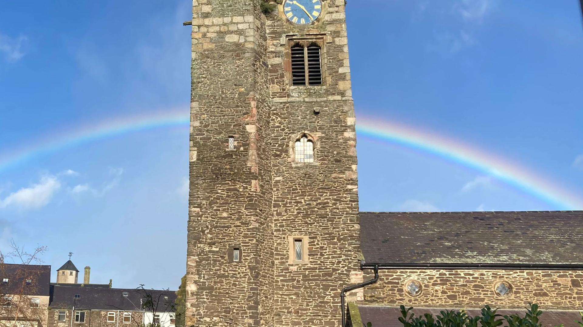 A stone church tower at Conwy St Mary with a rainbow behind it