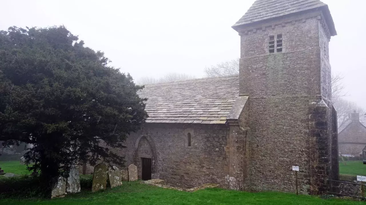 A grey stone church with a prominent square tower on the right of the image