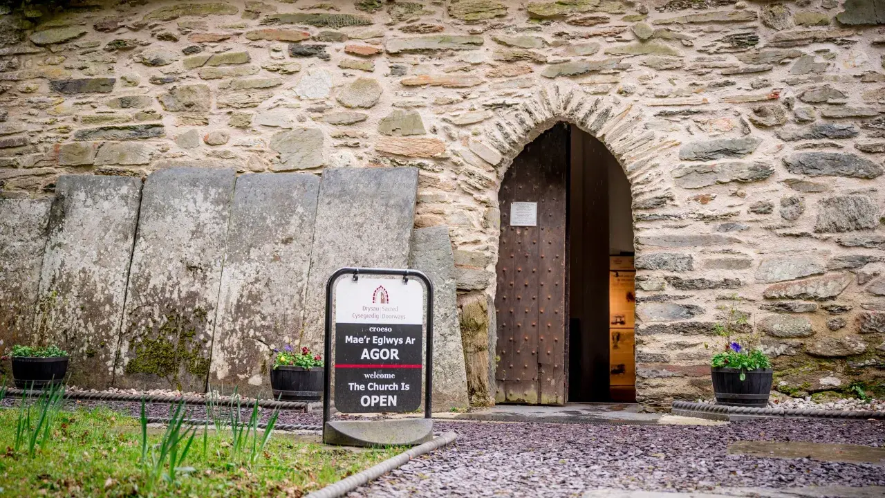 A bilingual sign welcomes people into an old stone church
