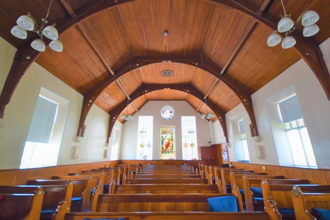 The interior of a church. Timber ceiling and pews with white walls. 