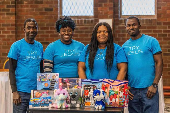 Four people stand inside RCCG Church in Edinburgh, with a table of gifts in front of them