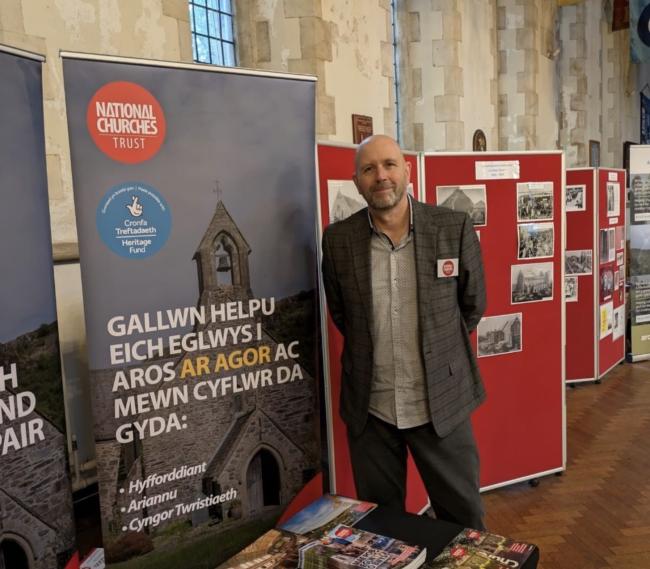 A man in a suit stands next to a pull up banner that in in Welsh