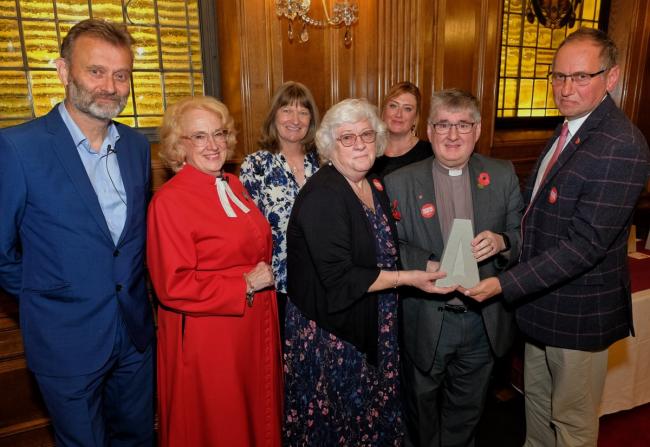A group of people stand in a room, facing the camera. Some of the people are holding an award.