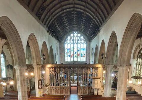 A photo of the interior of Totnes St Mary church looking at the stained glass window and altar and with arches to the side
