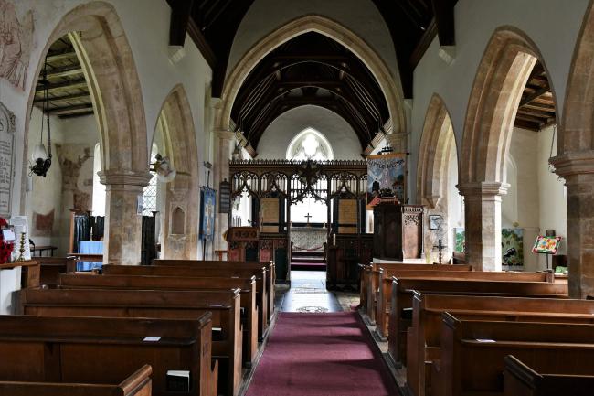 The inside of All Saints in Little Melton, Norfolk. Rows of pews face a reredos. There are arched columns either side of the pews.