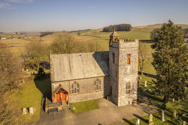 A Scottish church surrounded by greenery. There is a square tower on the right-hand side.
