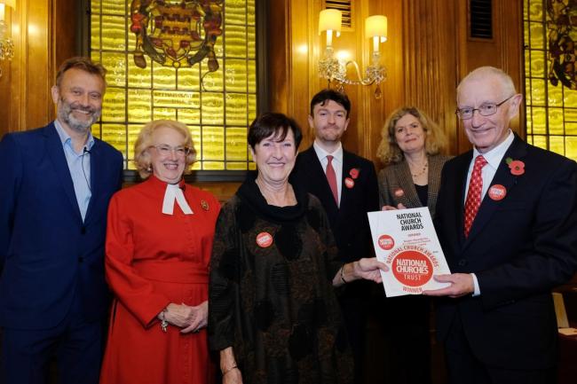 A group of people stand inside a room, one of them holding a certificate