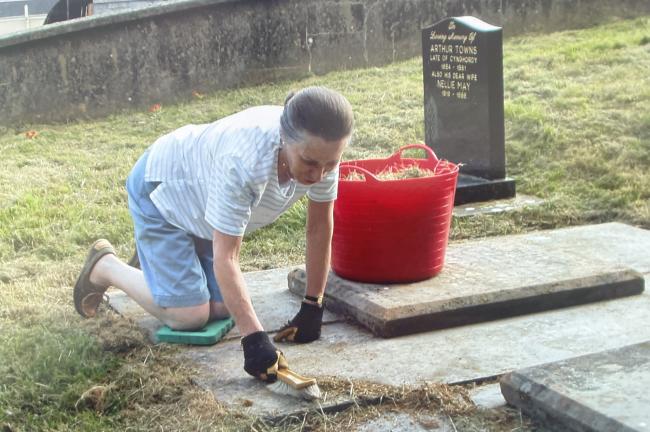 A woman brushes a stone clean in a churchyard