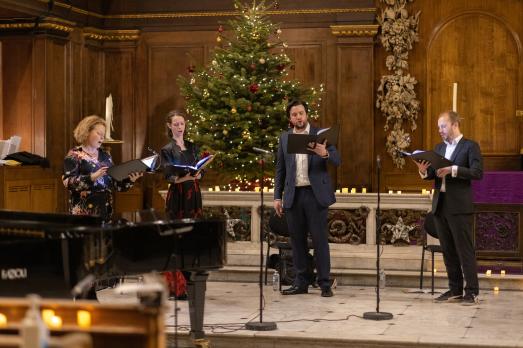 Four choristers singing in front of a Christmas tree in a church.