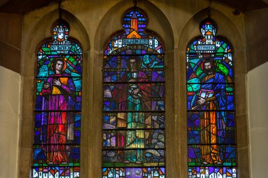 Colourful stained glass windows, depicting three figures, inside Dundela St Mark's Church in Belfast